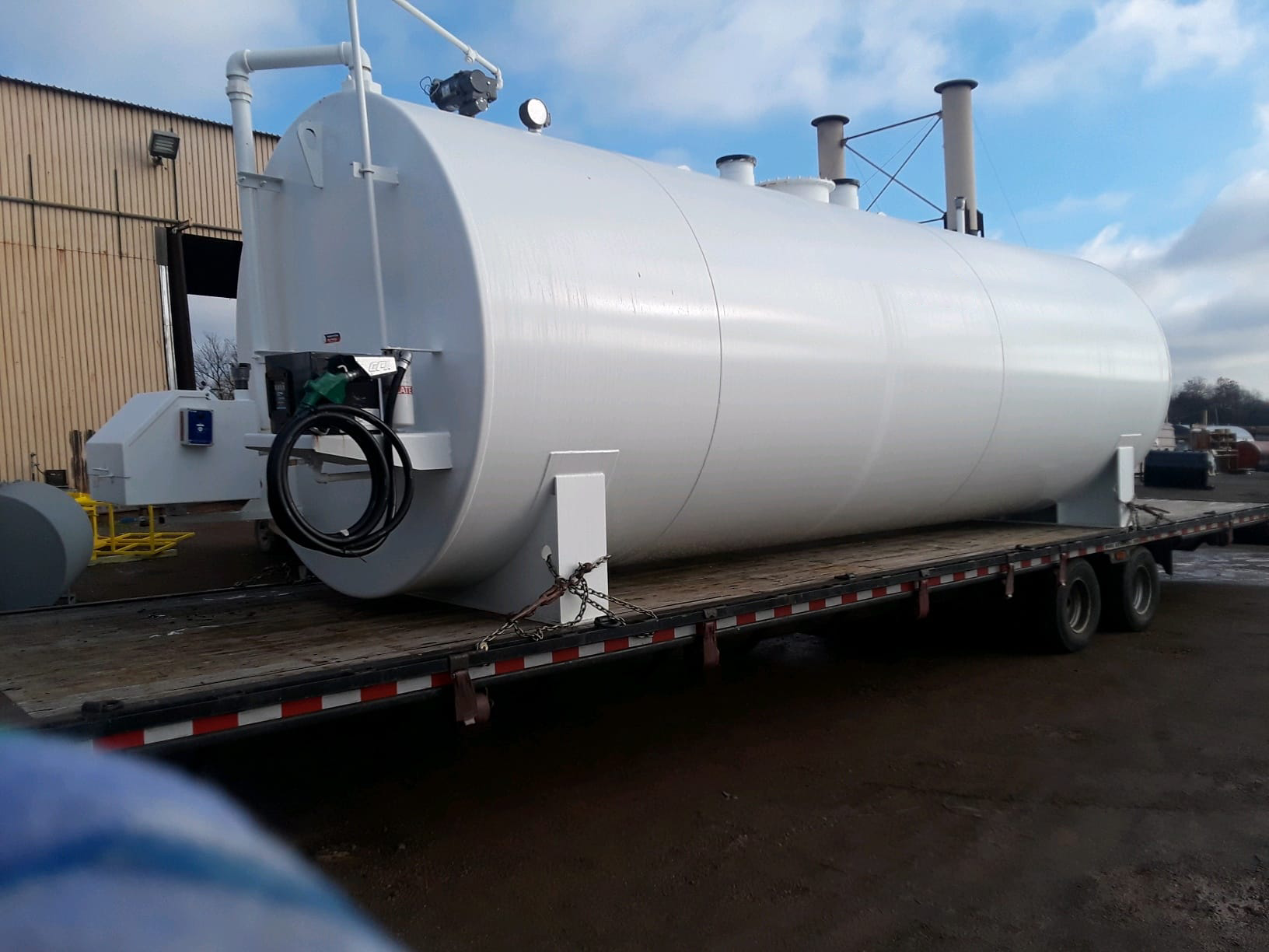 Large white double-walled fuel storage tank loaded on a flatbed trailer, ready for transportation to an industrial site.