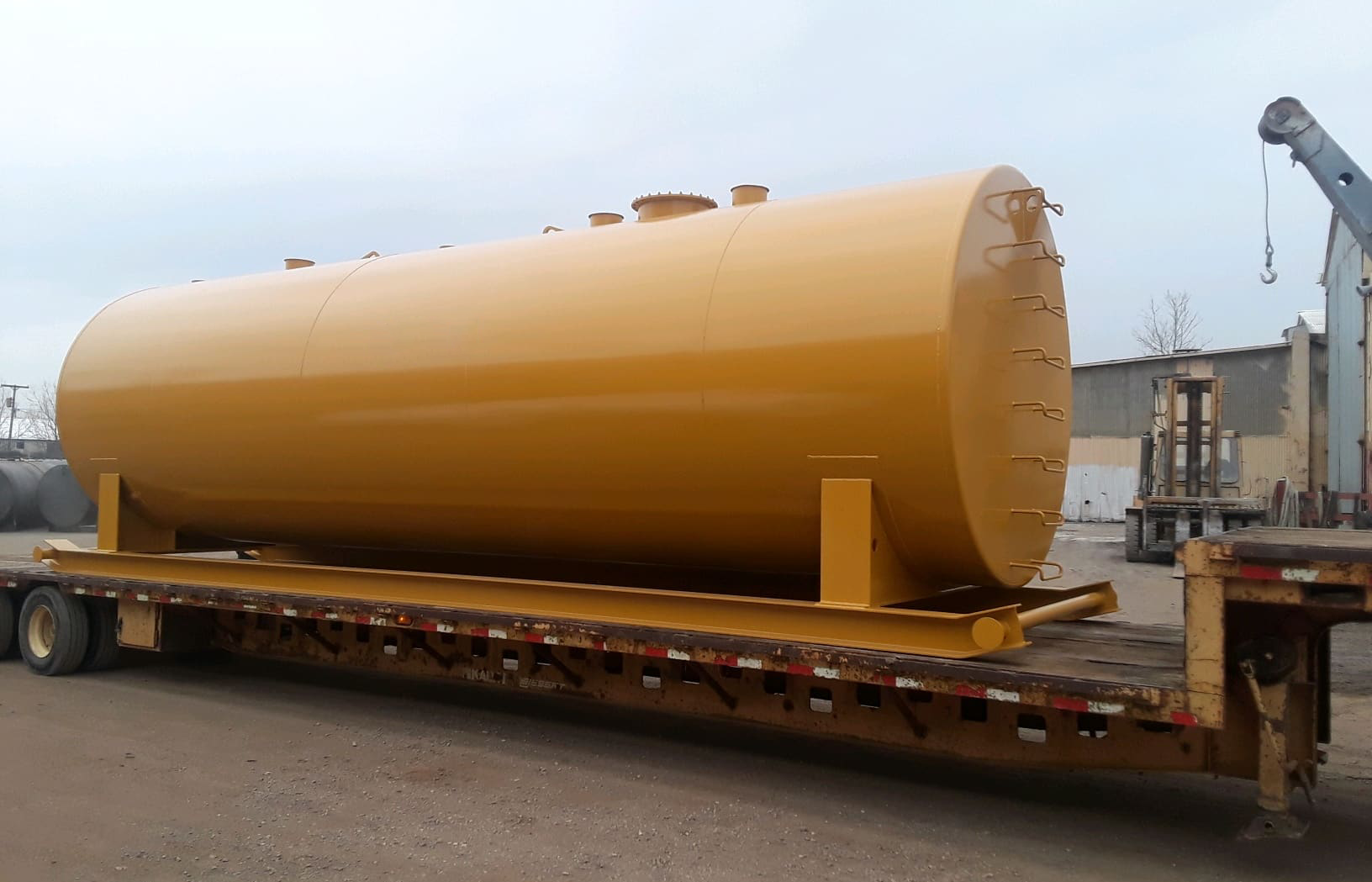 Yellow industrial fuel storage tank securely mounted on a flatbed trailer, designed for high-capacity fuel storage and transportation.