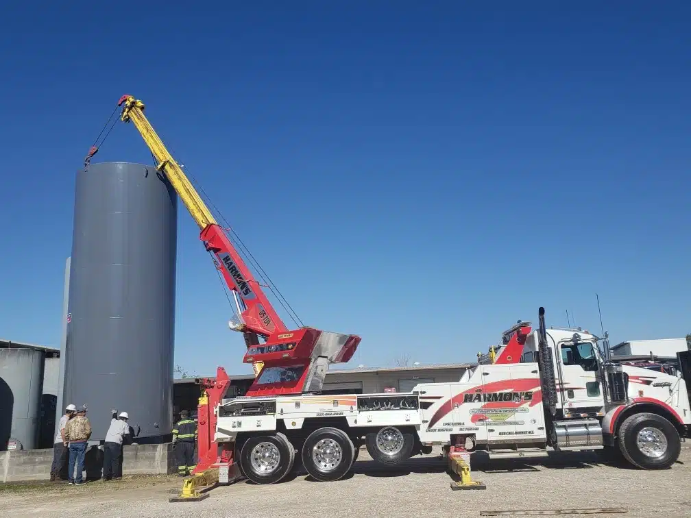 Large vertical fuel storage tank being installed by a crane on a construction site.