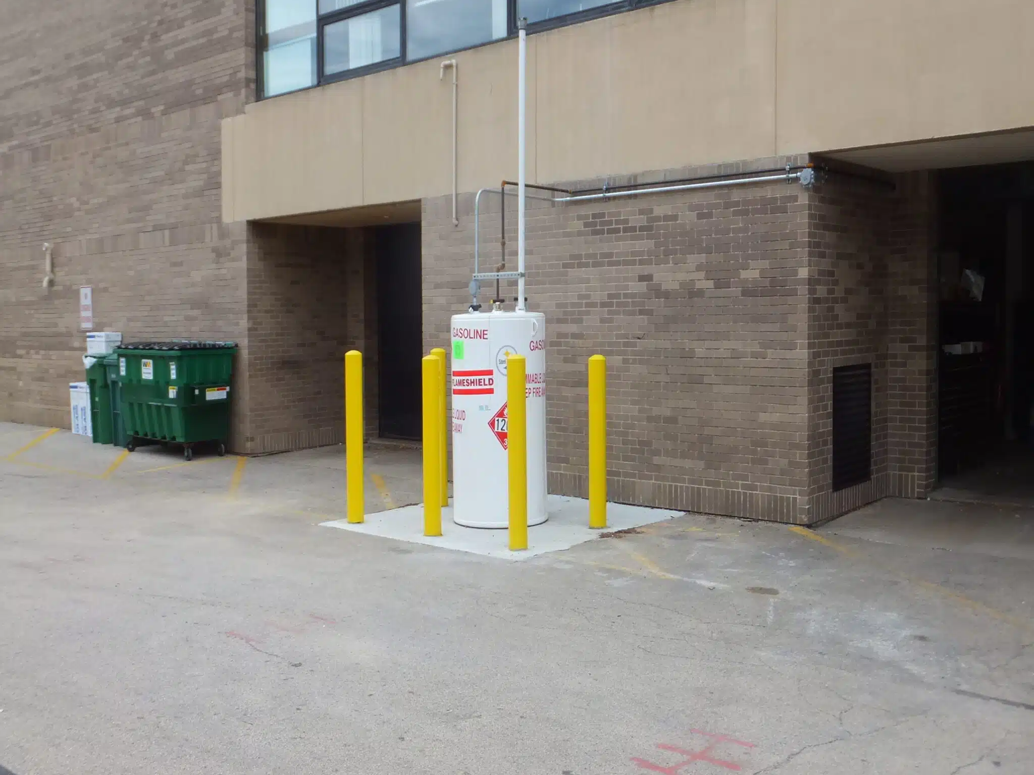 Small aboveground fuel storage tank installed outside a commercial building, secured with safety bollards.