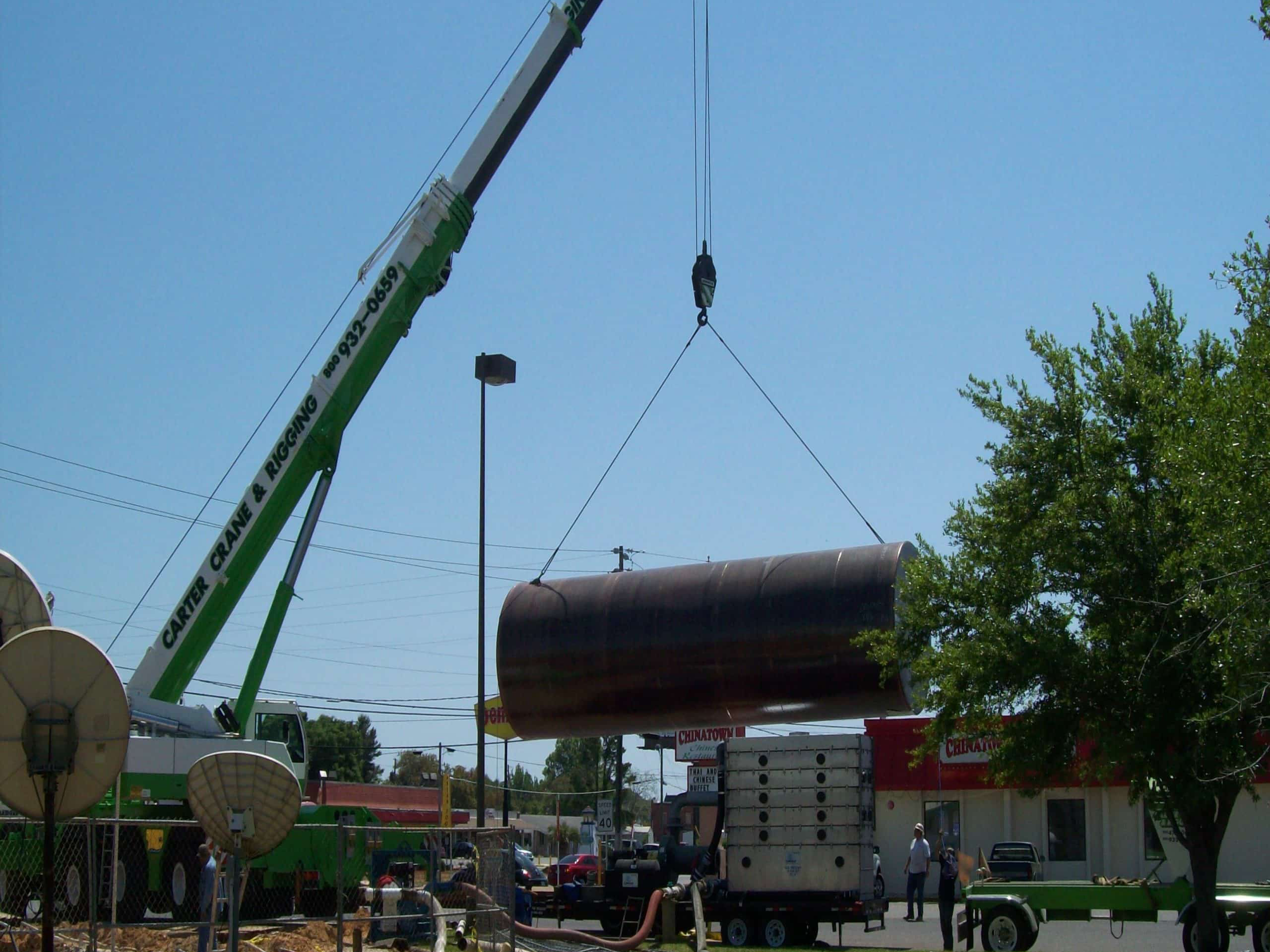 Installation of a large underground steel storage tank using a crane at a commercial site.